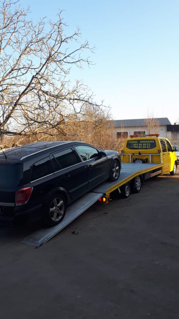 Laweta Polska przewożąca uszkodzony samochód na autostradzie, dostępna 24/7 w razie awarii lub wypadku.